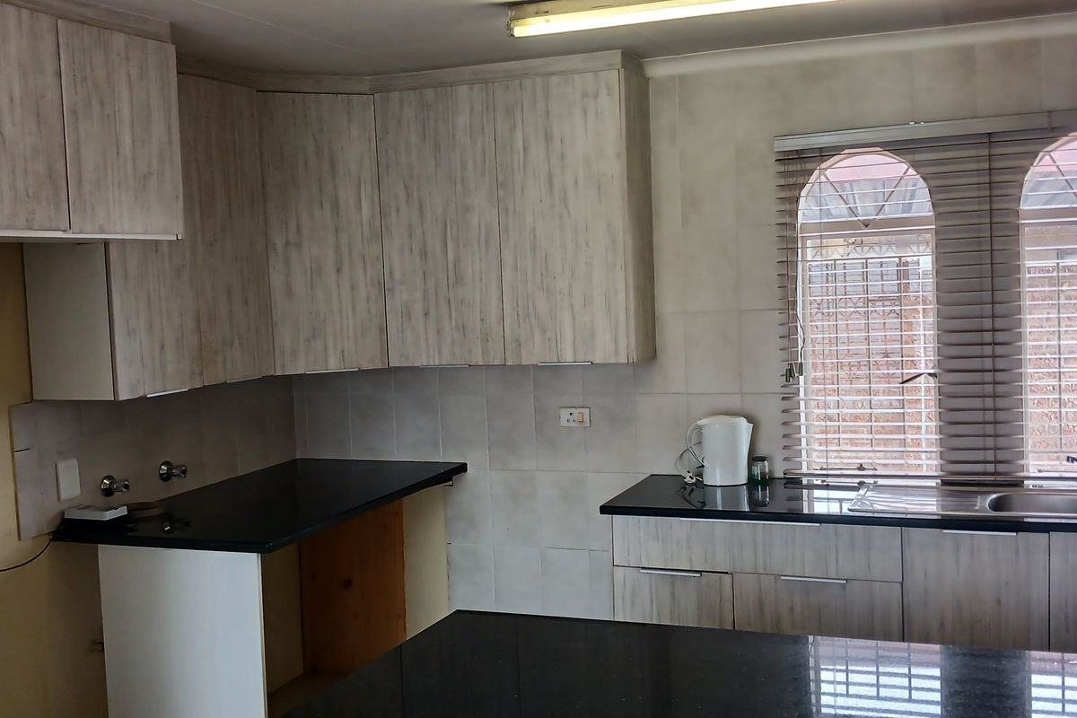 A functional kitchen featuring light wood-grain cabinetry, dark granite countertops, a double sink, and distinctive arched windows with fitted blinds.
