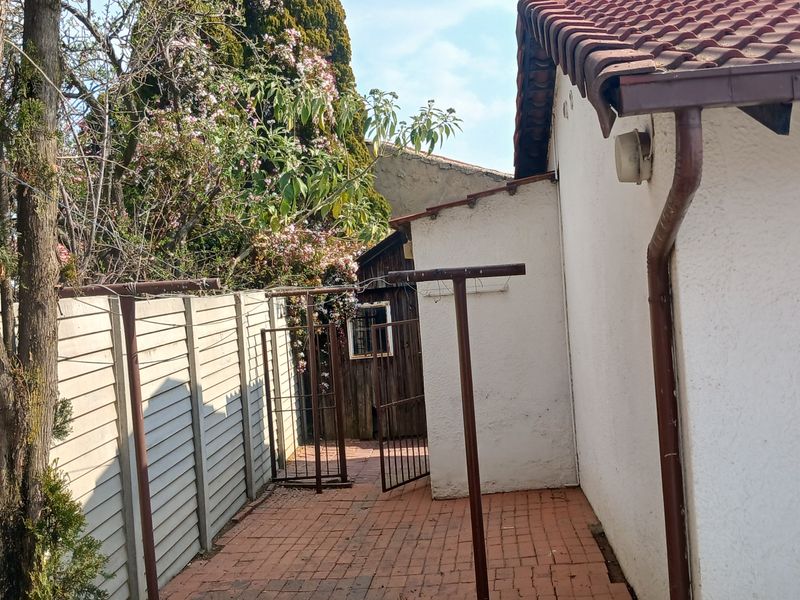A side exterior view of the property featuring brick paving, a precast concrete boundary wall, and a tiled roof with guttering.