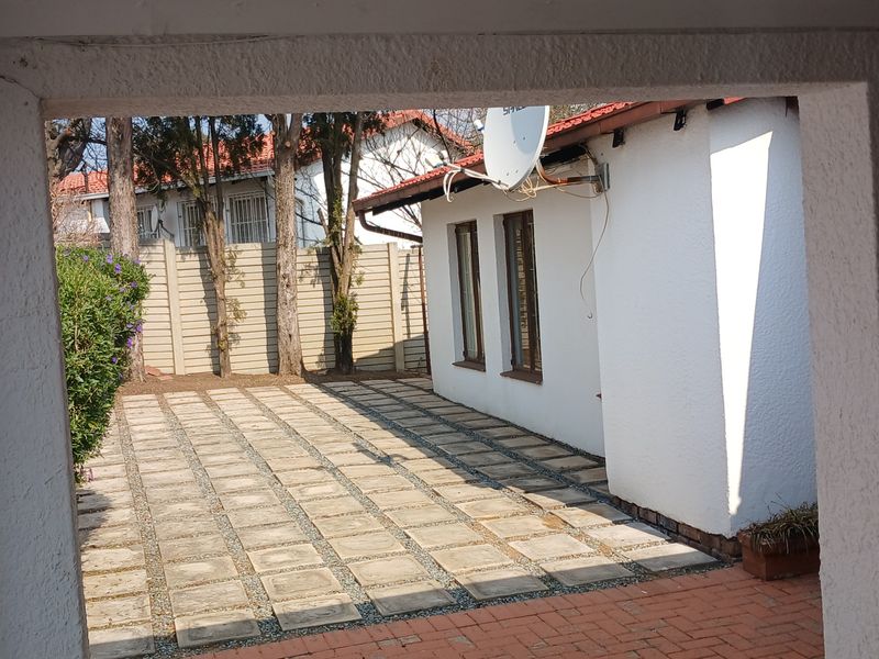 A view of the rear exterior area featuring a paved patio, brick pathways, and a precast concrete boundary wall.