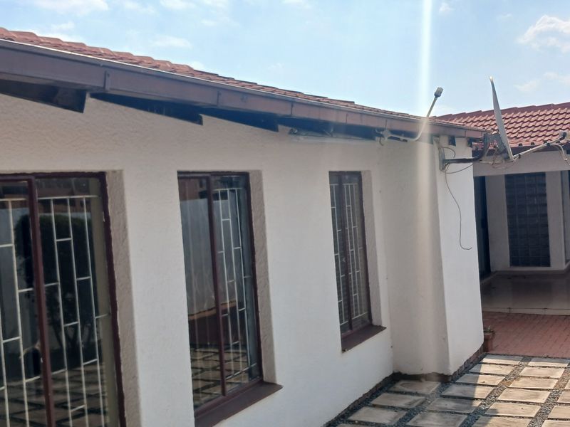 Rear exterior view of the house featuring a tiled roof, paved patio area, and security bars on the windows.