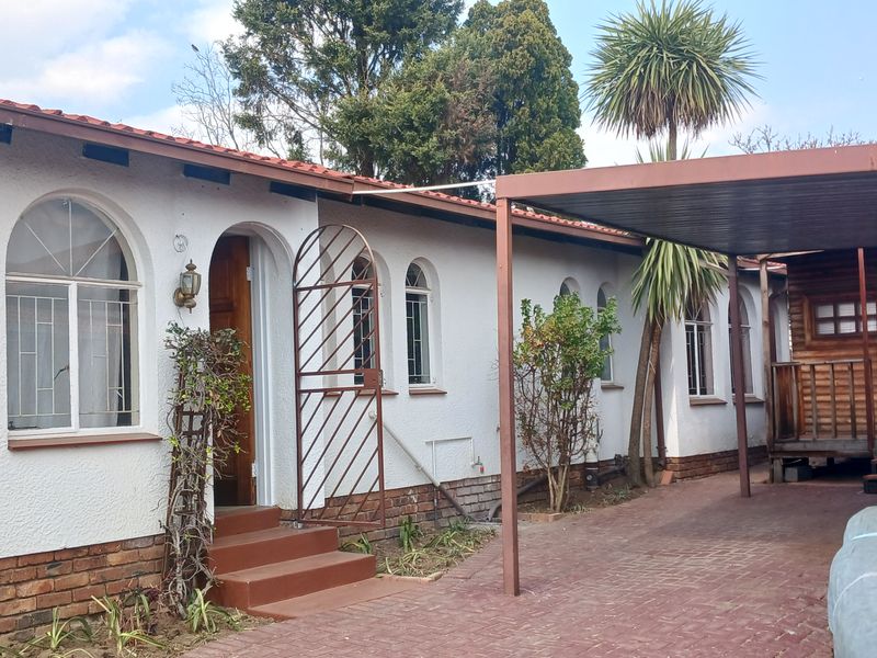 Front elevation of the house featuring a paved driveway, attached carport, arched windows, and secure entrance with security gate.