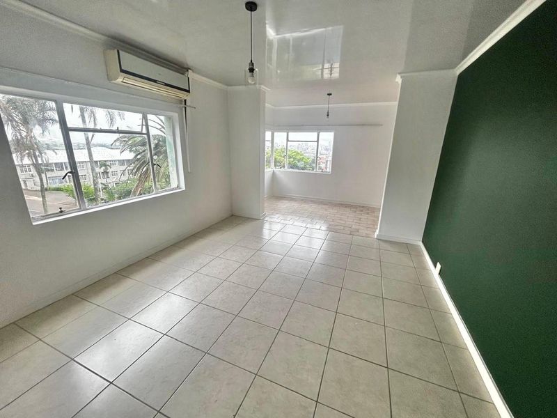 Spacious open-plan living area featuring tiled flooring, a split-system air conditioner, and a modern green accent wall with integrated lighting.
