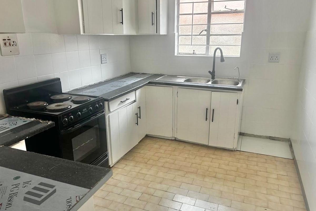 A functional kitchen featuring white cabinetry, dark countertops, a double basin sink, and a freestanding electric stove, ready for cosmetic updates.