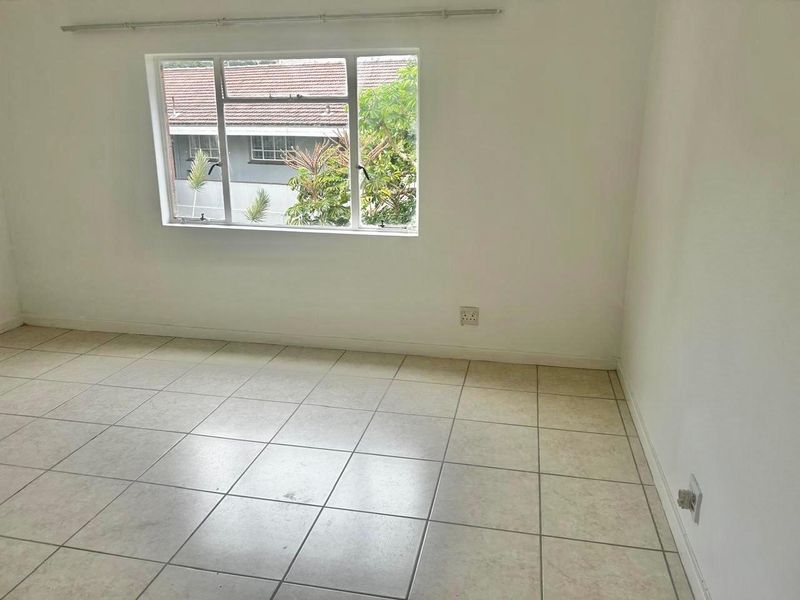 A bright, empty bedroom featuring neutral tiled flooring, a large window with an aluminium frame, and a wall-mounted curtain rail.