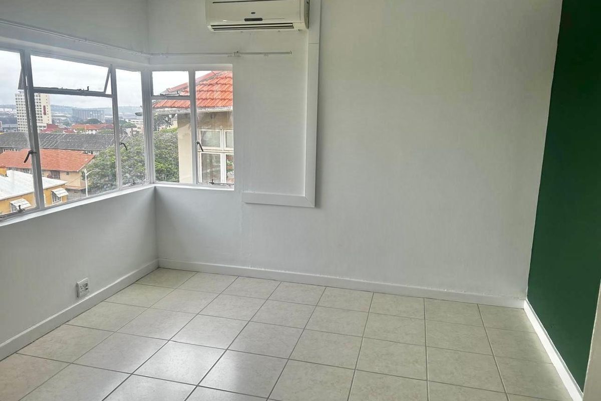 An empty bedroom featuring tiled flooring, a wall-mounted split-system air conditioner, and corner windows offering an elevated urban view.