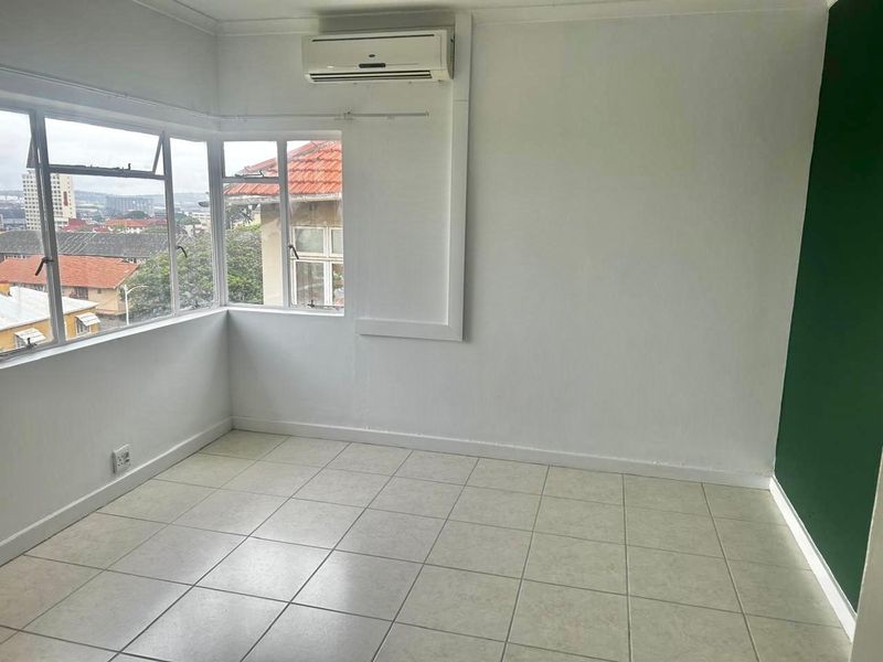 An empty bedroom featuring tiled flooring, a wall-mounted split-system air conditioner, and corner windows offering an elevated urban view.