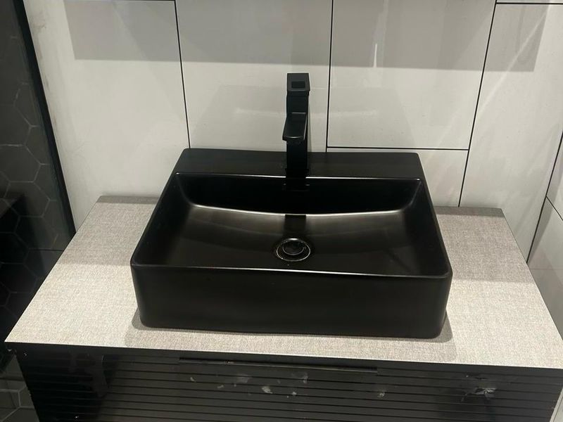 A modern bathroom vanity featuring a matte black vessel sink and matching mixer tap set against a tiled splashback.