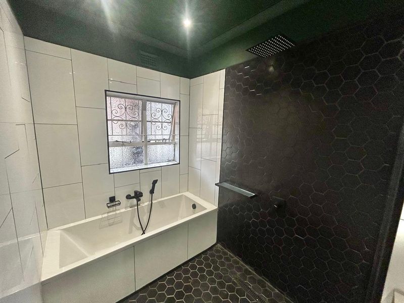 Modern bathroom featuring a built-in bathtub, a walk-in shower with a rain shower head, and contrasting black and white tiled finishes.