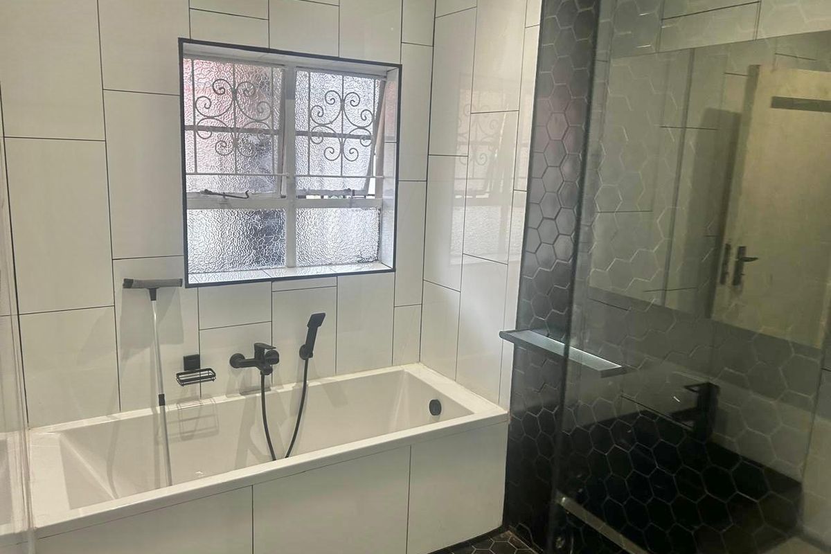 Modern bathroom featuring a built-in bathtub, separate shower enclosure with dark hexagonal tiling, and contemporary black fixtures.