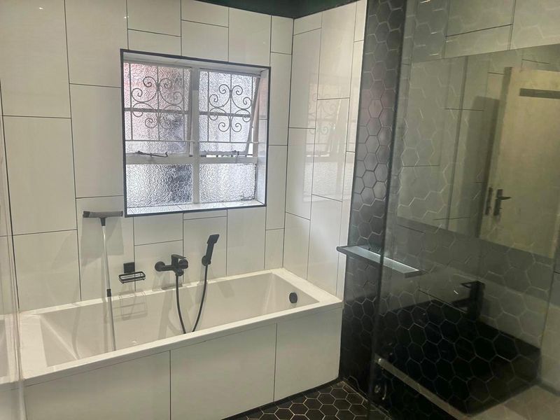 Modern bathroom featuring a built-in bathtub, separate shower enclosure with dark hexagonal tiling, and contemporary black fixtures.