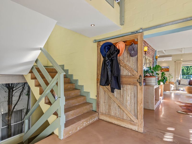 Entrance area featuring a timber staircase, painted brick walls, and a rustic sliding barn door leading into an open-plan living space.