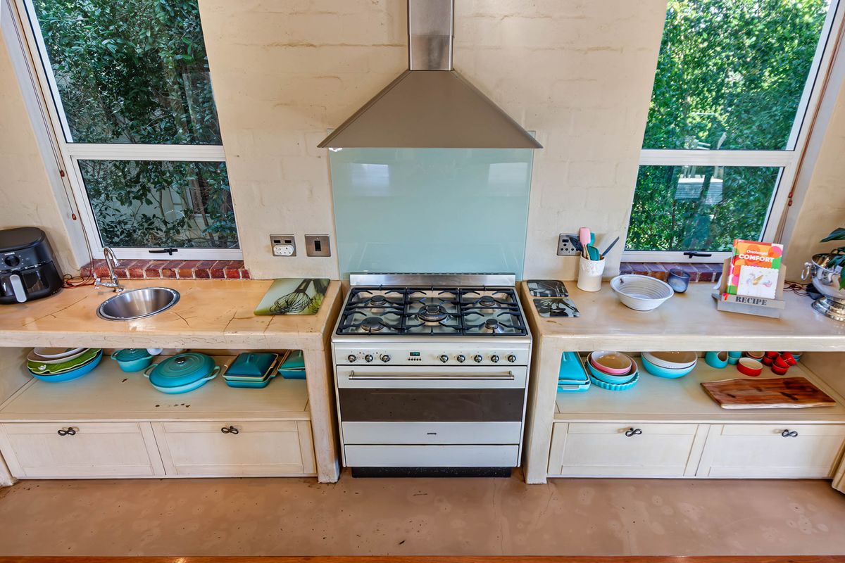 A rustic-style kitchen featuring a central gas stove with extractor fan, stone countertops, and integrated sink, set against a painted brick wall.