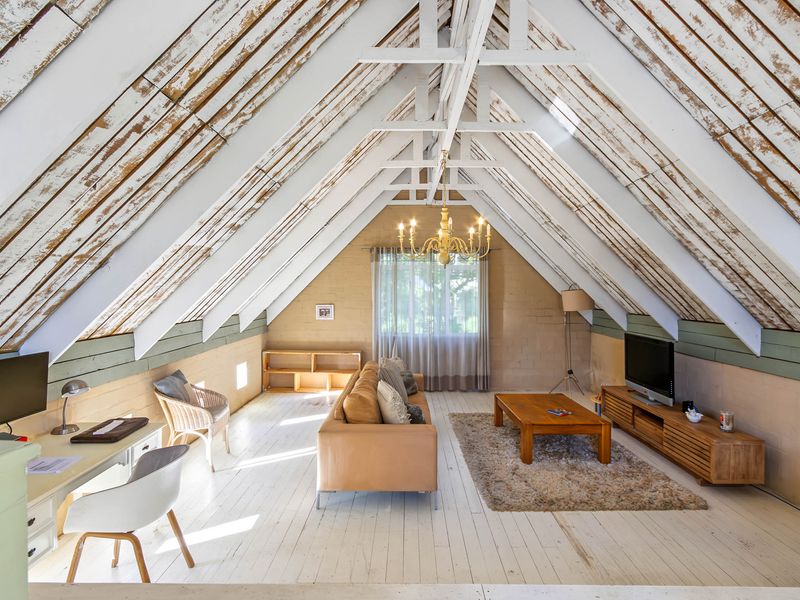 Spacious attic-style living room featuring exposed timber rafters, painted timber flooring, and brick walls, creating a rustic and character-filled living space.