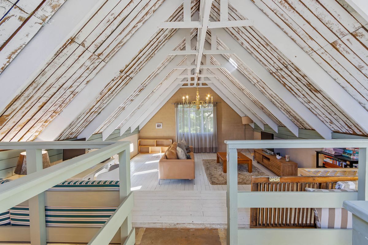 Spacious attic-style living room featuring a high vaulted ceiling with exposed timber rafters, white-painted wooden floors, and a mezzanine-level vantage point.