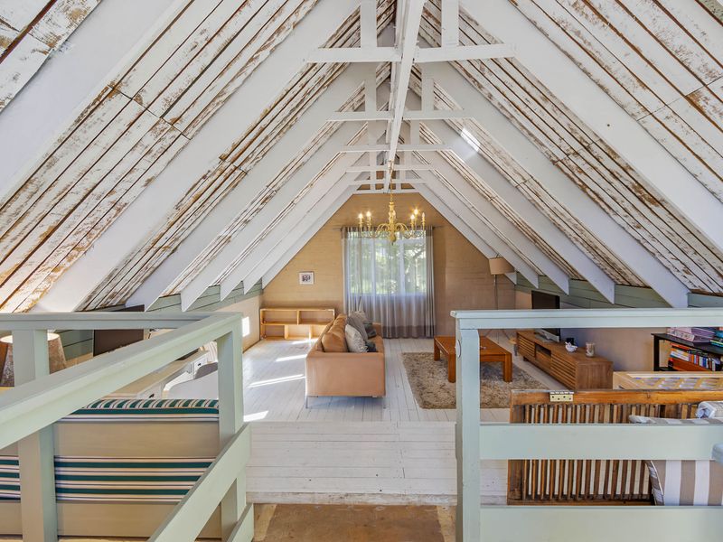 Spacious attic-style living room featuring a high vaulted ceiling with exposed timber rafters, white-painted wooden floors, and a mezzanine-level vantage point.