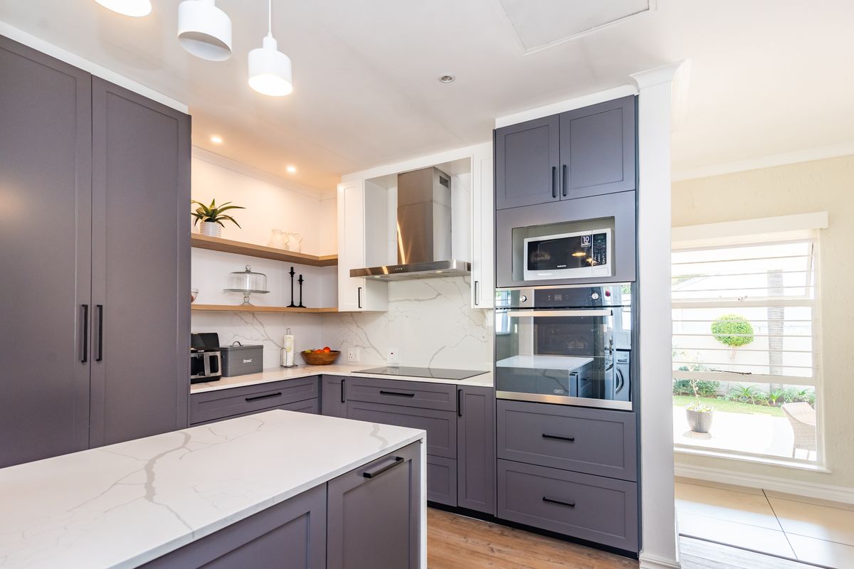 Modern kitchen featuring dark grey cabinetry, white stone countertops with marble veining, built-in appliances, and floating shelves, offering a sleek and functional cooking space.