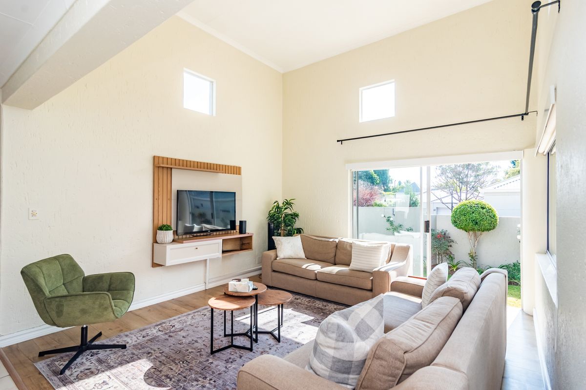 Bright living room featuring high vaulted ceilings, laminate flooring, and large sliding glass doors that provide seamless access to the outdoor patio area.