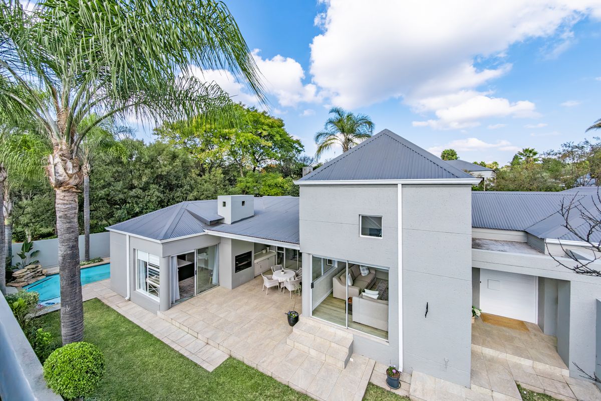 Rear view of the property featuring a spacious tiled patio with a built-in braai, overlooking a swimming pool and well-maintained garden.
