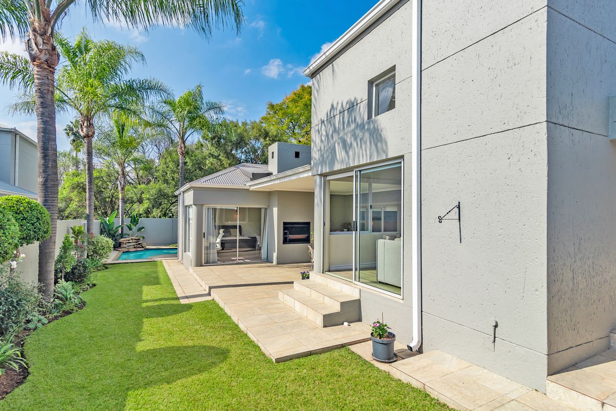 A well-maintained rear exterior featuring a tiled patio with a built-in fireplace, sliding doors, and a landscaped garden with a swimming pool.