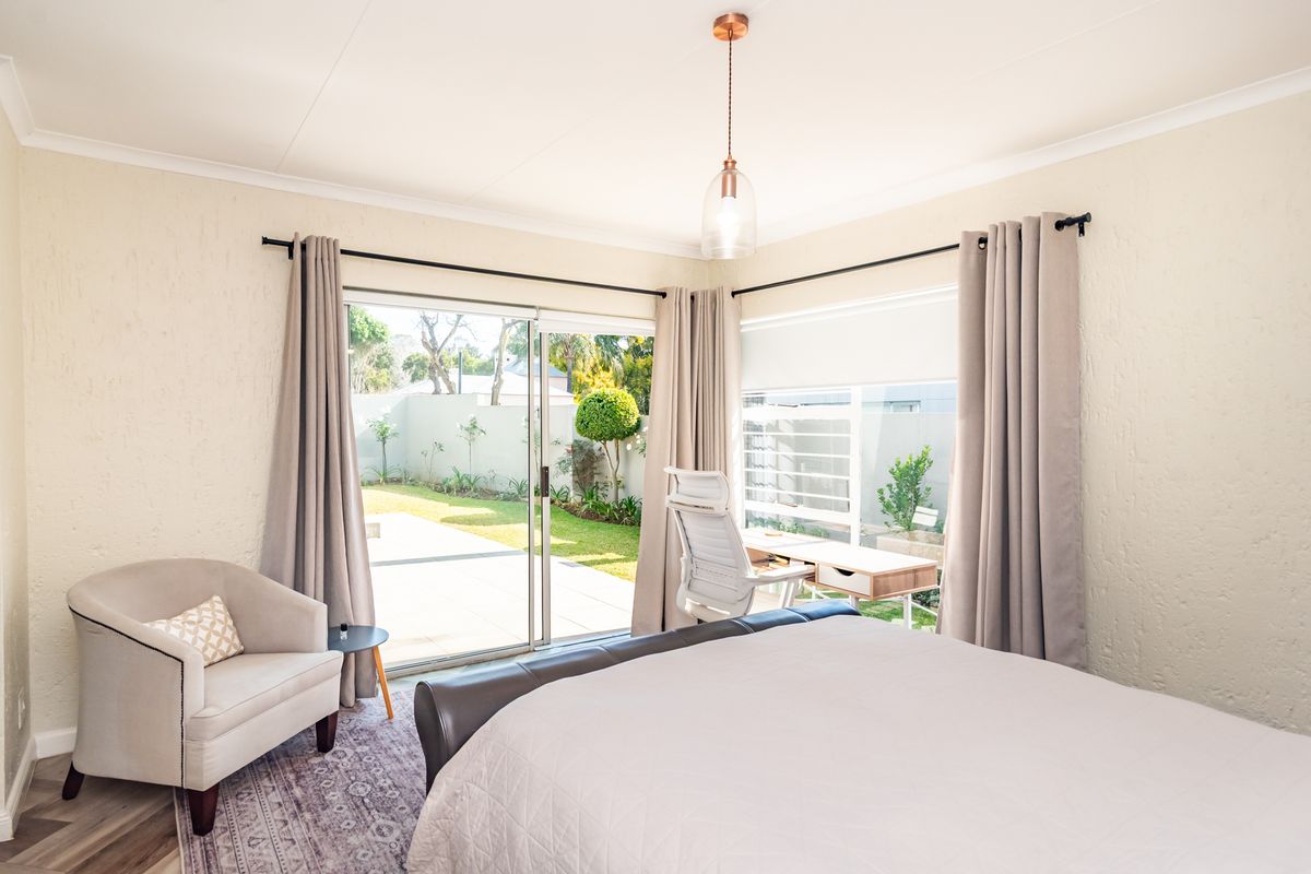 Bright bedroom featuring textured walls, laminate flooring, and a sliding glass door providing direct access to the rear garden and patio area.