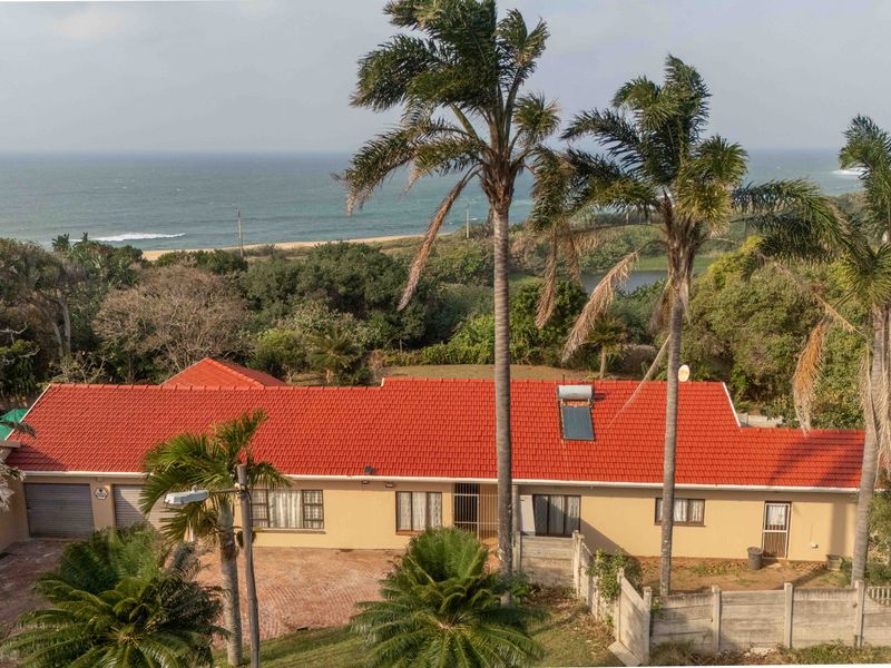 Aerial view of a coastal property featuring a tiled roof with solar water heating, a paved driveway, and a garage, set against a scenic ocean backdrop.