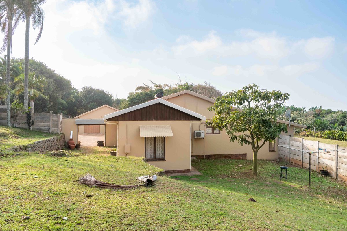 Rear view of the house featuring a spacious garden, concrete boundary walls, and a detached garage structure.