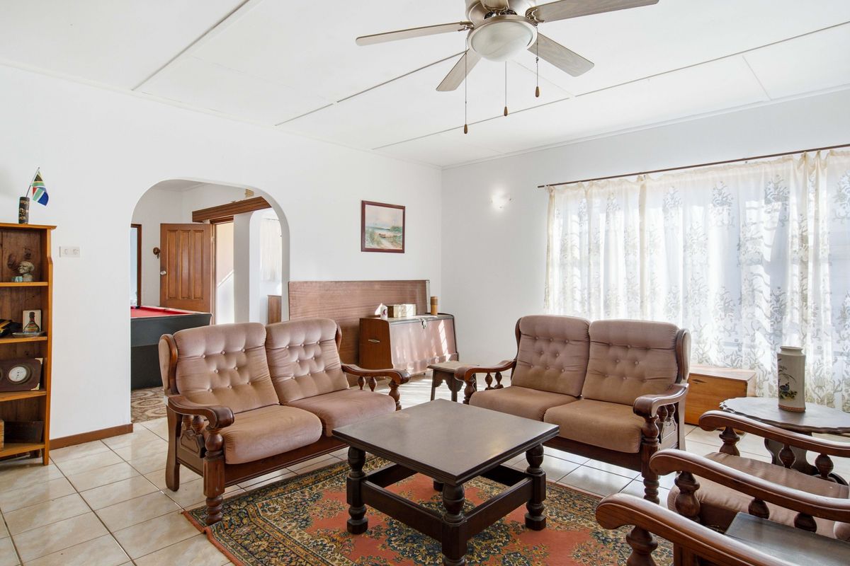 A spacious living room featuring tiled flooring, a ceiling fan, and an arched entryway leading to an adjacent room.