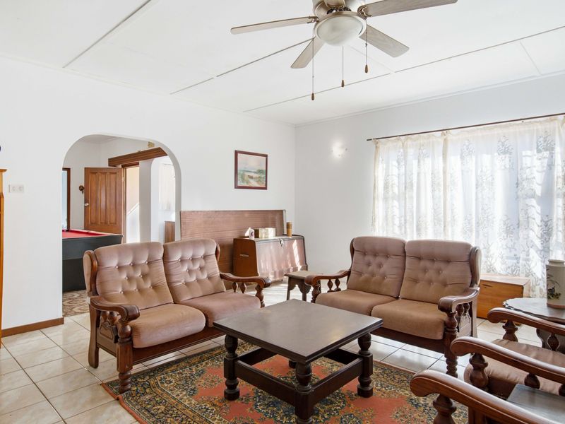 A spacious living room featuring tiled flooring, a ceiling fan, and an arched entryway leading to an adjacent room.