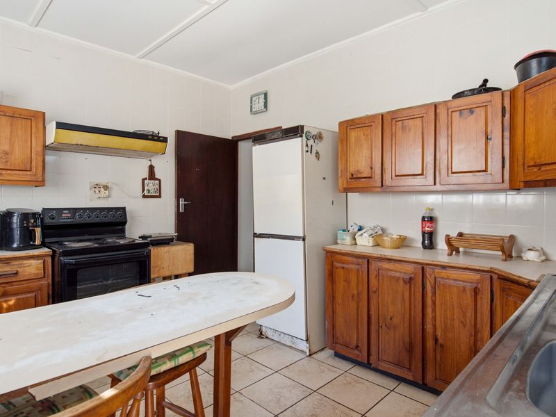 A dated kitchen featuring wooden cabinetry, tiled splashbacks, and a built-in oven, offering significant potential for modernization and renovation.