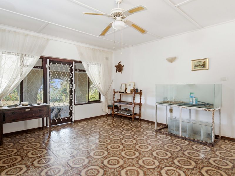 A spacious living area featuring patterned tile flooring, a ceiling fan, and a sliding door with a security gate leading to the exterior.