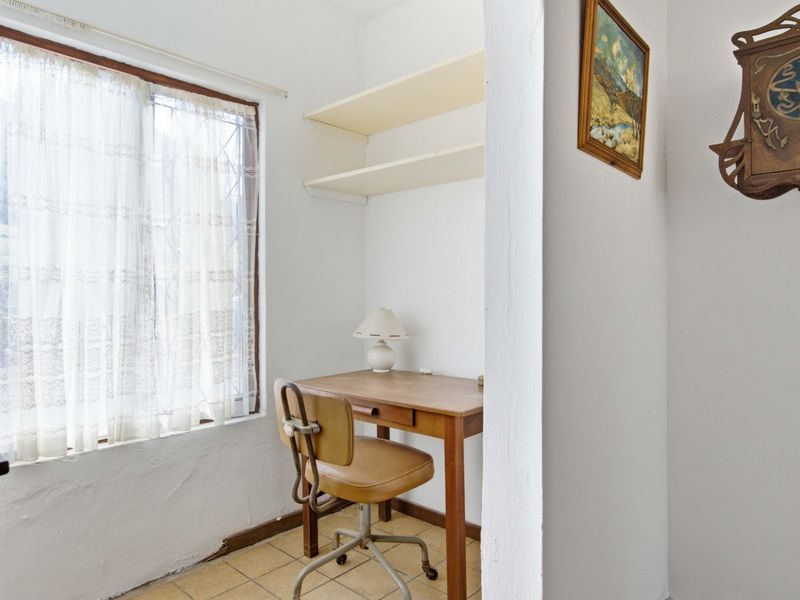 A small office nook featuring built-in shelving and tiled flooring, offering a functional workspace with natural light from the window.