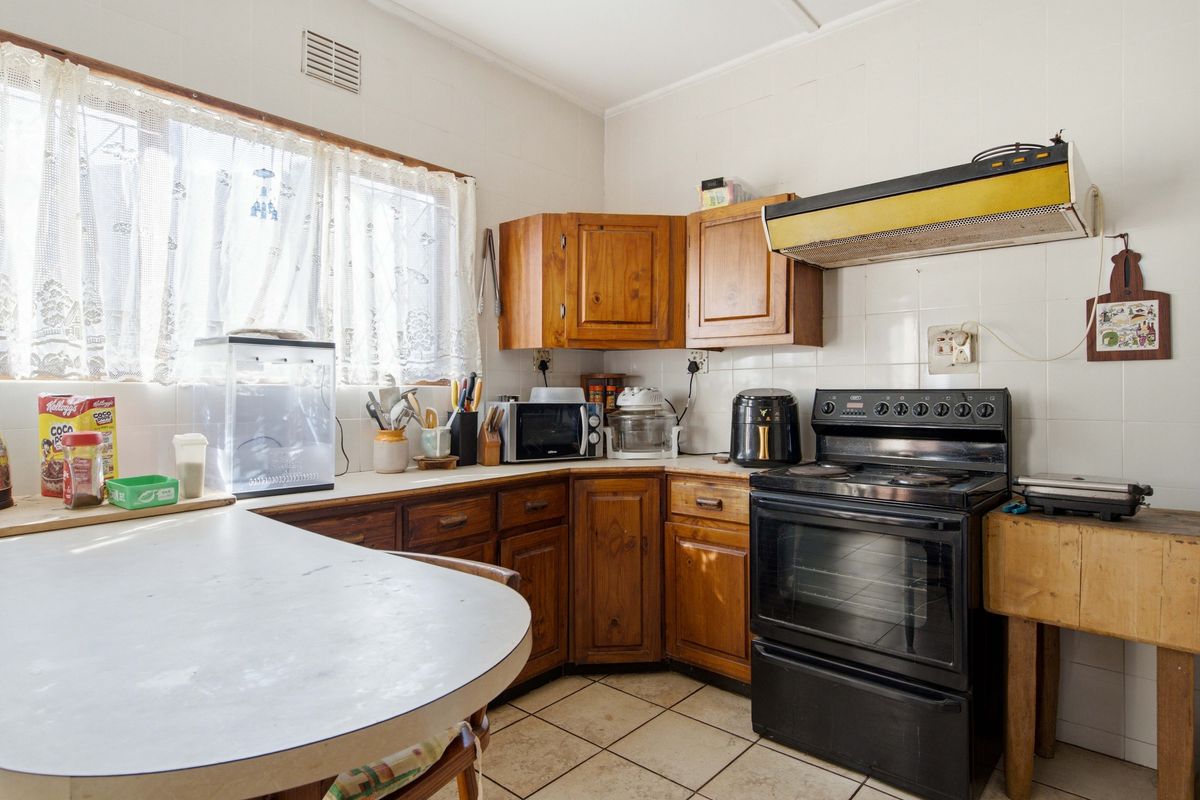 A dated kitchen featuring wooden cabinetry, tiled splashbacks, and a freestanding oven, offering significant potential for a modern renovation.