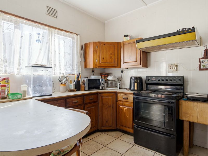 A dated kitchen featuring wooden cabinetry, tiled splashbacks, and a freestanding oven, offering significant potential for a modern renovation.