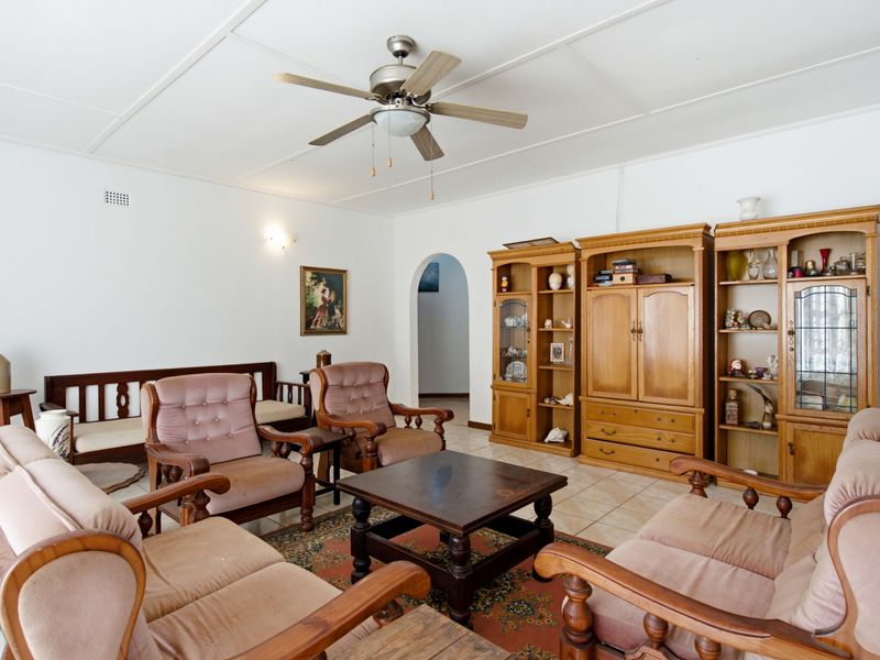 A spacious living room featuring tiled flooring, a ceiling fan, and an arched entryway leading to other areas of the home.