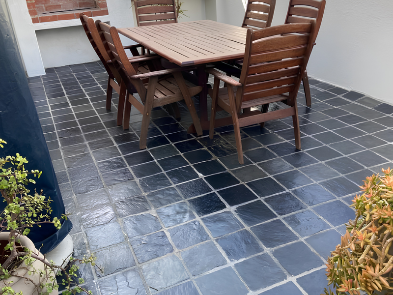 A private outdoor patio featuring a built-in brick fireplace, dark stone tile flooring, and a metal balustrade, ideal for outdoor dining and entertaining.