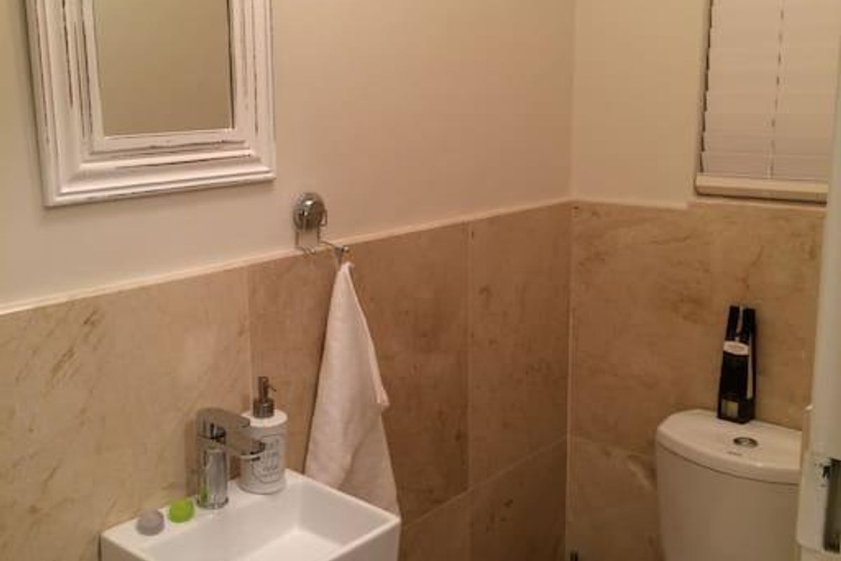 A compact guest bathroom featuring a wall-mounted basin, modern chrome tapware, and neutral stone tiling throughout.
