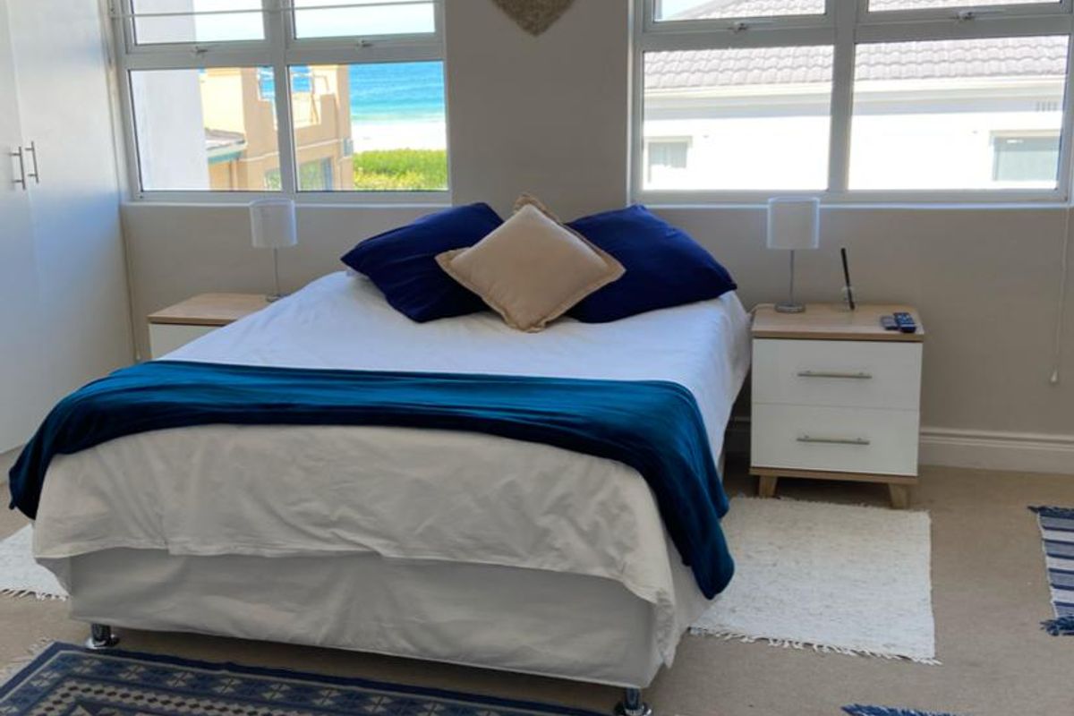 A bright bedroom featuring built-in cupboards, neutral carpeting, and large windows offering natural light and coastal views.