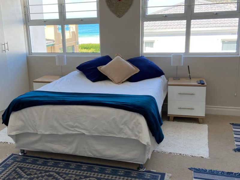 A bright bedroom featuring built-in cupboards, neutral carpeting, and large windows offering natural light and coastal views.