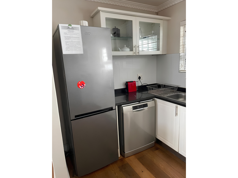 A compact kitchen area featuring white cabinetry, stone countertops, a stainless steel sink, and integrated dishwasher with modern finishes.
