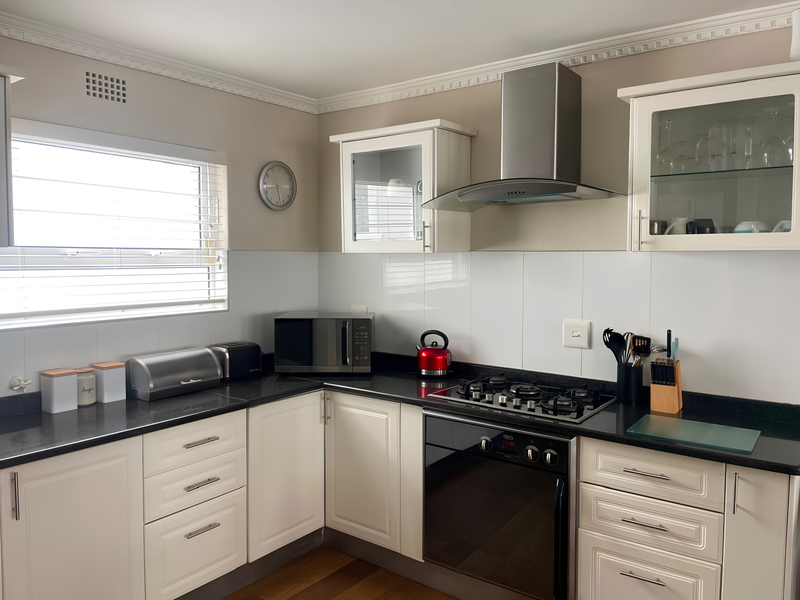 A well-maintained kitchen featuring white cabinetry, dark granite countertops, a gas hob, built-in oven, and a stainless steel extractor fan.