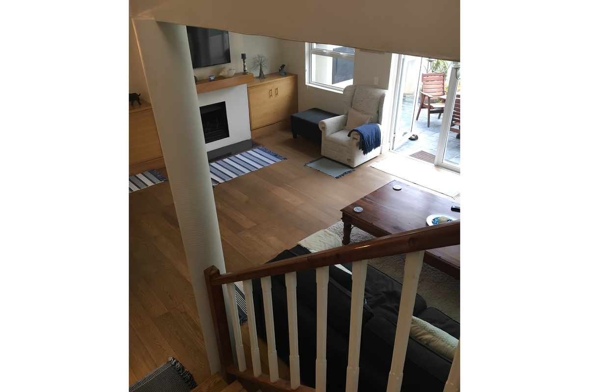 A view from the staircase looking down into a living room featuring hardwood floors, a fireplace with built-in cabinetry, and access to an outdoor patio.