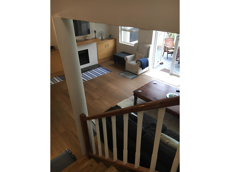 A view from the staircase looking down into a living room featuring hardwood floors, a fireplace with built-in cabinetry, and access to an outdoor patio.
