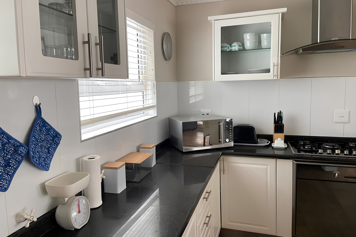 A well-maintained kitchen featuring white cabinetry, dark granite countertops, a built-in oven, gas hob, and a stainless steel extractor fan.