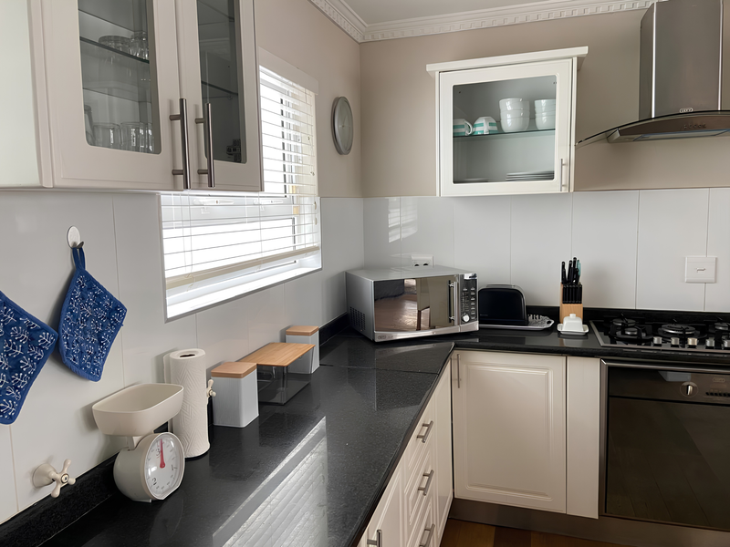 A well-maintained kitchen featuring white cabinetry, dark granite countertops, a built-in oven, gas hob, and a stainless steel extractor fan.