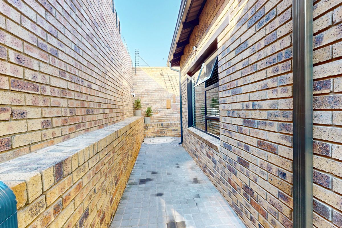 A side passage featuring face brick walls, a paved walkway, and an aluminium window frame, providing access along the side of the property.