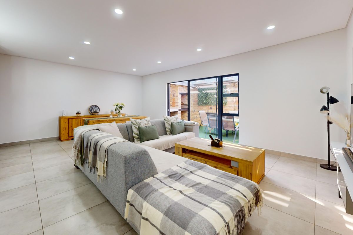 Spacious living room featuring neutral tiled flooring, recessed downlighting, and large sliding glass doors providing seamless access to the outdoor patio area.