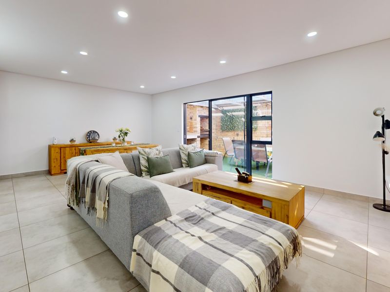 Spacious living room featuring neutral tiled flooring, recessed downlighting, and large sliding glass doors providing seamless access to the outdoor patio area.