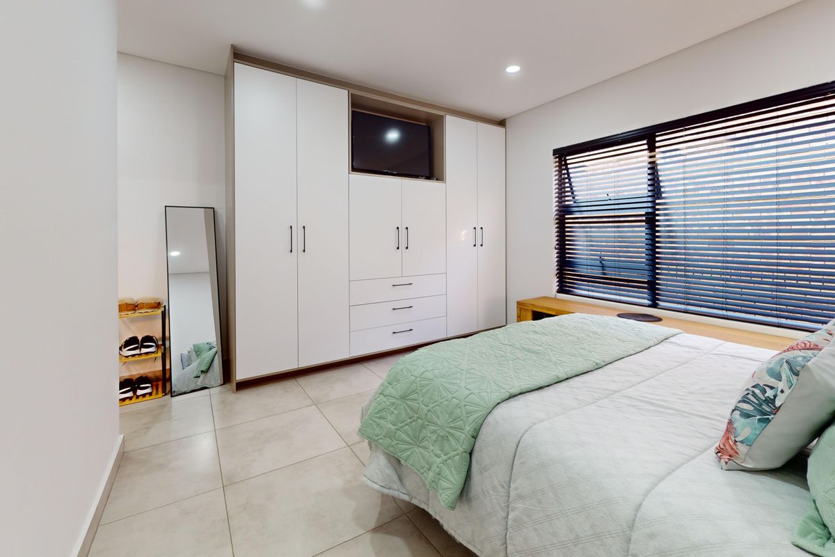 A well-maintained bedroom featuring modern built-in cupboards, neutral tiled flooring, and venetian blinds, offering a clean and functional living space.