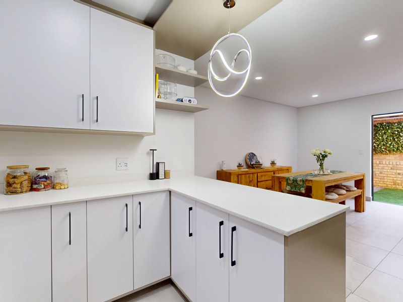 Modern open-plan kitchen and dining area featuring sleek white cabinetry, stone countertops, and seamless access to a private rear patio.