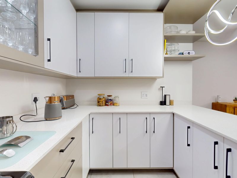 A modern, well-maintained kitchen featuring clean white cabinetry, stone countertops, and contemporary pendant lighting, offering a bright and functional workspace.